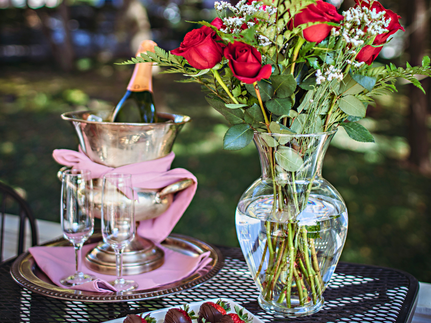 A bush of red roses next to a cooled bottle of wine