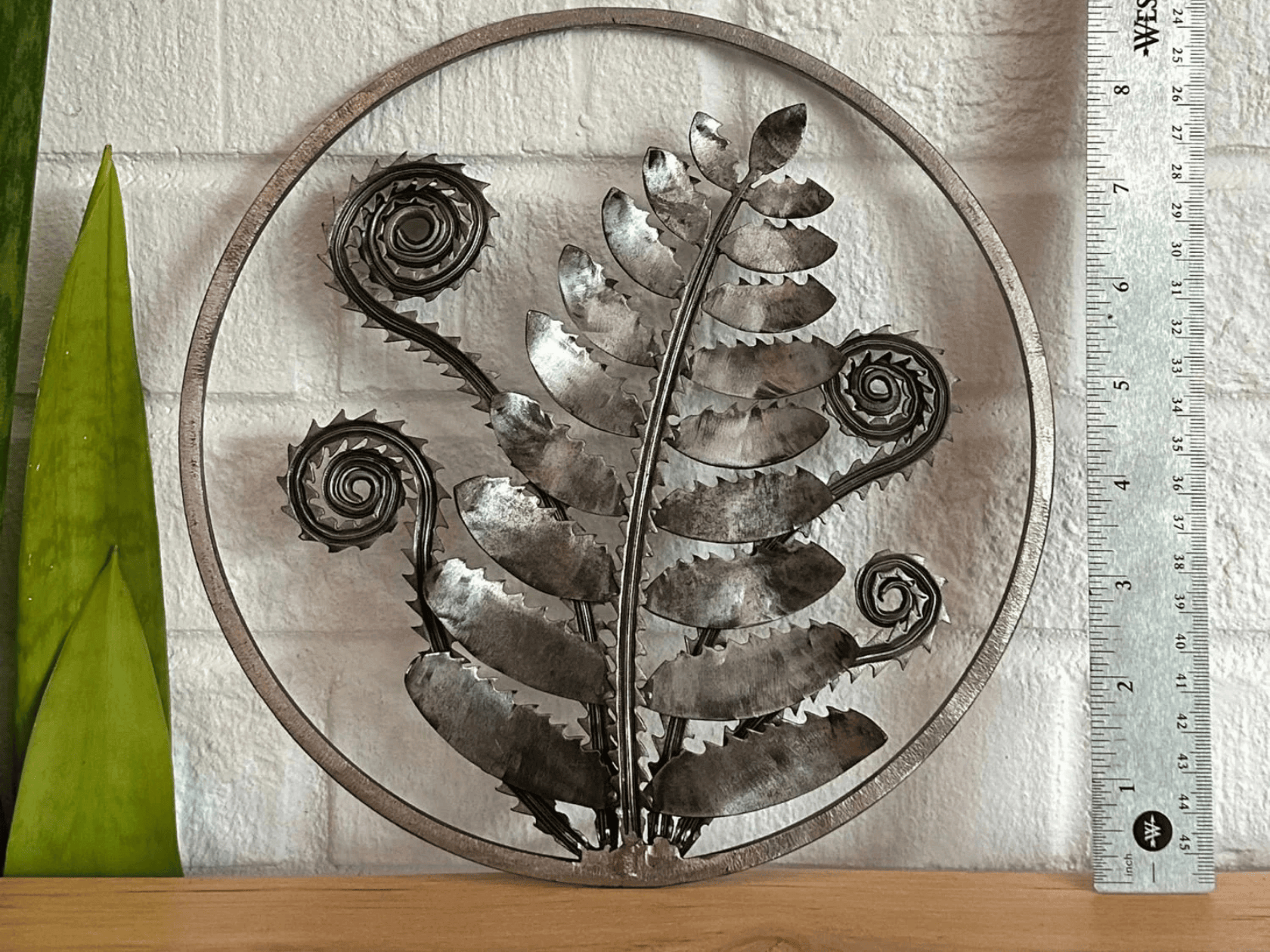 A silver plated wall decor with a fern and vines 